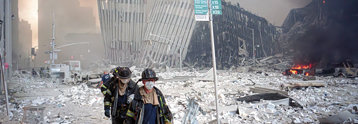 dazed looking firefighters walking through jagged dusty wreckage of a collapsed building