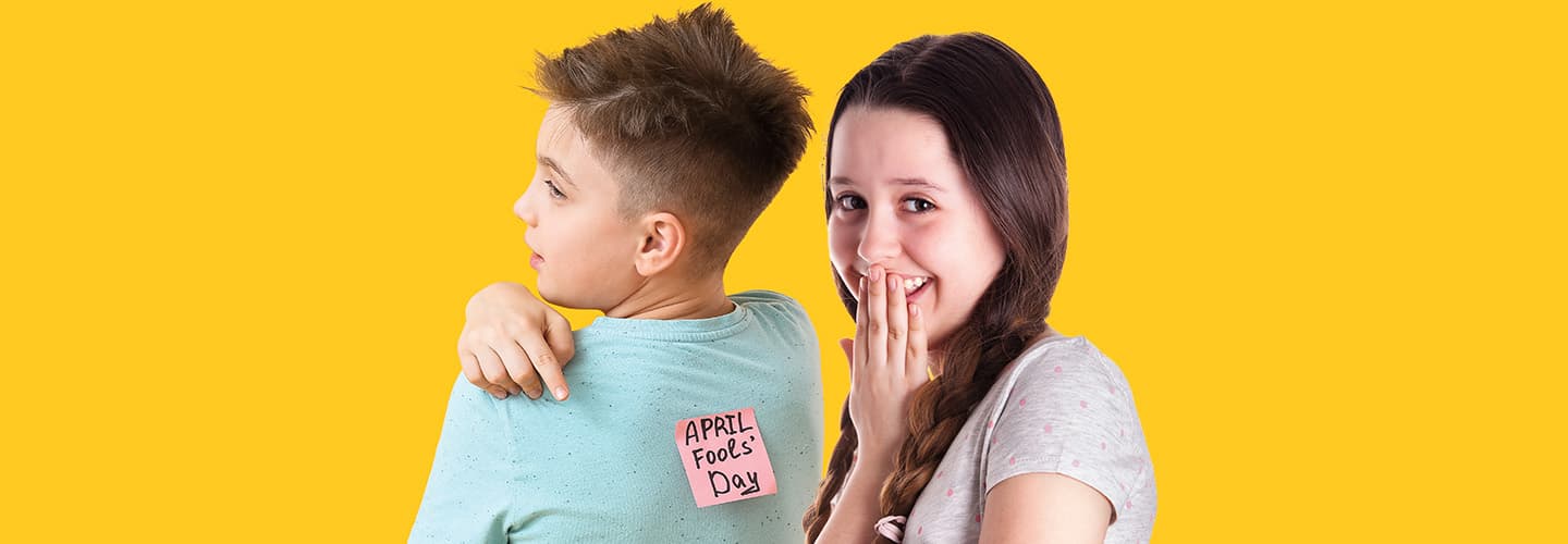 Image of one friend putting an &apos;April&apos;s Fool Day&apos; note on someone&apos;s back
